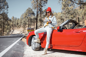 Naklejka premium Woman having a snack with lunch box while standing on the roadside near the car, traveling on the mountains