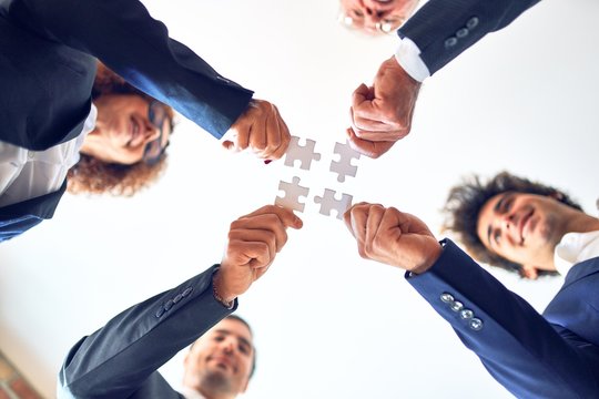 Group of business workers smiling happy and confident. Standing on a circle with smile on face trying to connect puzzle pieces at the office.