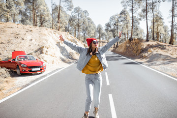 Lifestyle portrait of a carefree woman running on the beautiful mountain road, having a stop while traveling by car on the island. Happy road trip concept