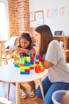 Beautiful teacher and toddler girl playing with construction blocks bulding tower at kindergarten