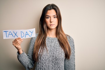 Young beautiful girl holding paper with tax day message standing over white background with a...