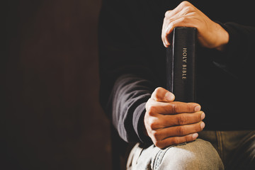 Casual man praying with his hands together with Holy Bible.