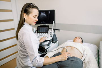 Pretty female doctor operating modern ultrasound scanner while examining belly and bladder of her female patient