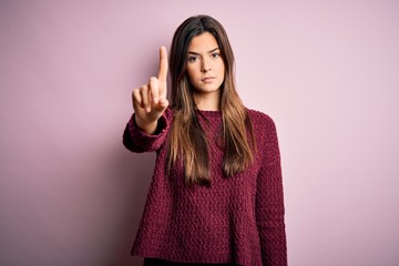 Young beautiful girl wearing casual sweater over isolated pink background Pointing with finger up and angry expression, showing no gesture