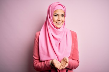 Young beautiful girl wearing muslim hijab standing over isolated pink background Smiling with hands palms together receiving or giving gesture. Hold and protection