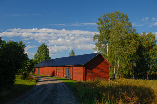 old red barn with black roof beside a gravel country road