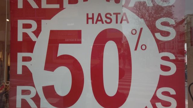 Tilt Up of Half Off Sale Sign in Shop Window with Spanish Rebajas Writing