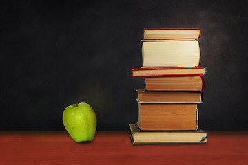 Back to school, pile of books and green apple with empty green school board background, education concept