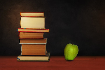 Back to school, pile of books and green apple with empty green school board background, education concept