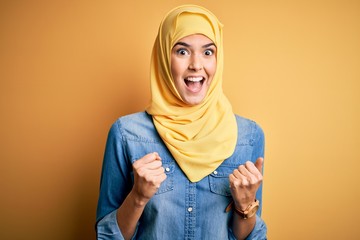 Young beautiful girl wearing muslim hijab standing over isolated yellow background celebrating surprised and amazed for success with arms raised and open eyes. Winner concept.