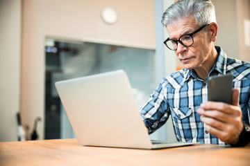 Adult man with smartphone working at laptop