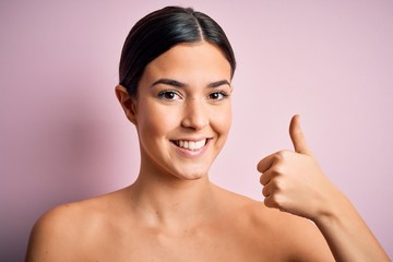 Young beautiful girl standing over isolated pink background happy with big smile doing ok sign,...