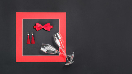 Framed red bow tie earings and flute sparkling wine glasses. Flat lay on black background. 14 February. Passion, love and feelings St Valentine's Day Card celebration concept with copy space
