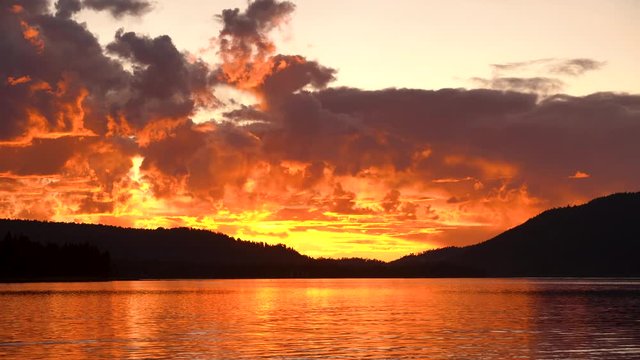 Big Bear Lake, fire Sunset with lake reflection, mountains and trees in the background, dramatic clouds floating through the sky. Wide shot of sunset and sky. 4K, Thirty seconds long.