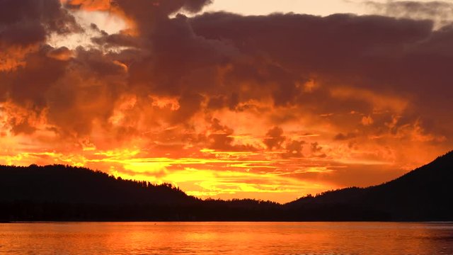 Big Bear Lake, fire Sunset with lake reflection, mountains and trees in the background, dramatic clouds floating through the sky. Close up of sunset and sky. 4K, nine seconds long.