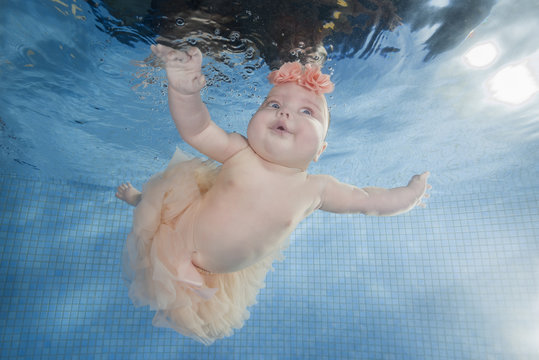 Cute chubby little girl dives underwater in a swimming pool