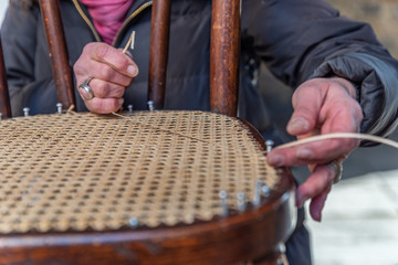 The hands of an artisan weave the wooden chair