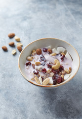 Bowl of granola with yogurt, nuts, cranberry and cocoanut on bright stone  background.