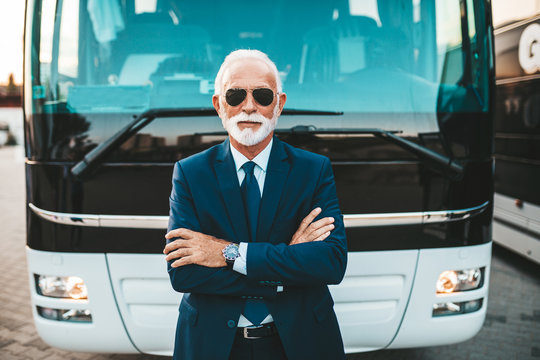 Mature beard bus driver standing in front of bus.