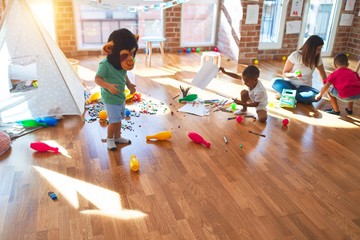 Young beautiful teacher and toddlers playing around lots of toys at kindergarten