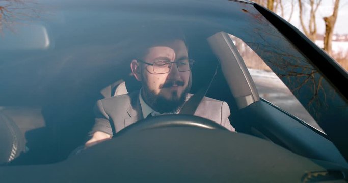 Good looking young Caucasian man driving a car on a sunny morning while going to the work and enjoying a view from a window.