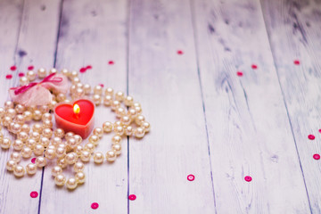 on a white wooden background red candle pearl beads