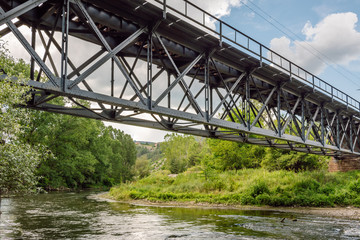 View of an old iron railway bridge over a river with lush green vegetation along its banks.