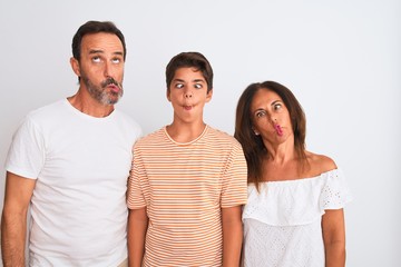 Family of three, mother, father and son standing over white isolated background making fish face...