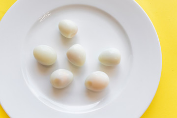 Set of peeled organic small boiled quail eggs on white plate on yellow background. Top view, copy space. Healthy protein fresh natural food. Natural gourmet meal. Little bird eggs. Close up photo.