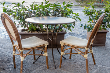 Fototapeta na wymiar Brown metal empty table and two old wooden chairs are outside by the potted green plants in the morning