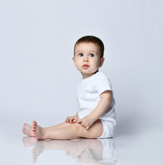 Portrait in profile of calm newborn baby boy toddler sitting sideways on the floor looking at us on a gray