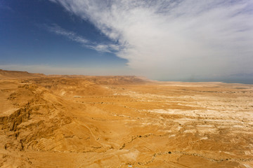 Fototapeta na wymiar Desert of Israel near the Dead Sea. The dried earth and stones bathed in the sun at its zenith. Over the desert horizon white clouds. Beautiful desert view of travel routes