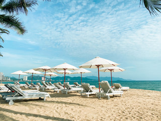 White soft sun loungers on the shore of a sandy sea beach. Tropical resort