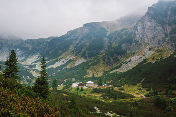 View of a green mountain valley with а refuge, steep rocky slopes, covered with coniferous shrubs...