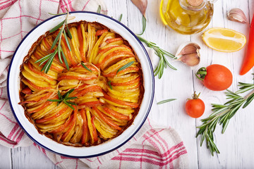 Slices of potato backed with tomatoes and onion, decorated with rosemary. Top view. Vegetarian dish. 