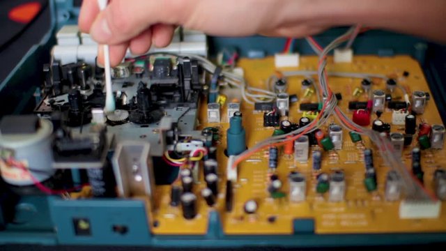 Cleaning the dust form the main circuit board inside of an old multi track analog tape recorder for a miniature audio engineering studio set up.
