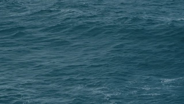Cinematic aerial shot of dark blue ocean surface, moody sea waves, deep ocean