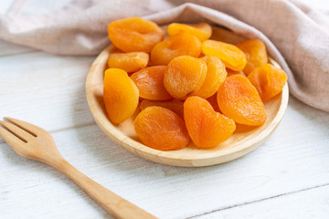 Dried apricots in wooden plate     on white wooden background with table cloth and fork, close up.