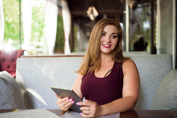 Obraz premium Everyday look. Plus size model. Beautiful young woman with a tablet in a restaurant.