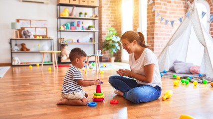 Fototapeta premium Beautiful teacher and toddler boy building pyramid with hoops bolcks at kindergarten