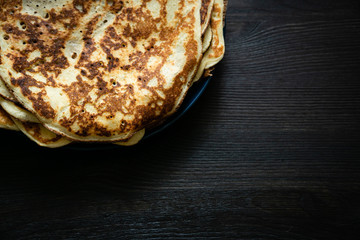 Thin pancakes in a round plate on a dark wooden surface. Nutritious breakfast of flour and eggs.