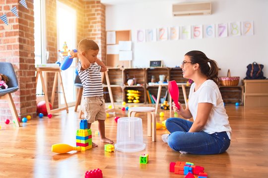 Beautiful teacher and toddler boy playing drum using skitlle and plastic basket at kindergarten