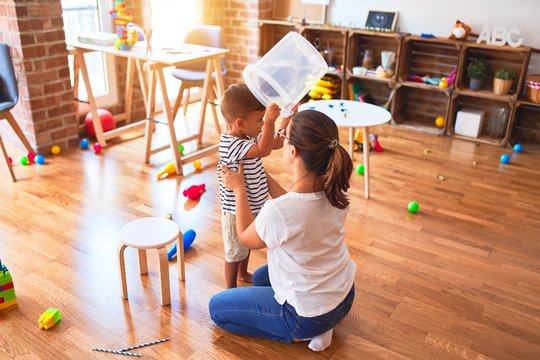 Beautiful teacher and toddler boy playing with plastic basket at kindergarten