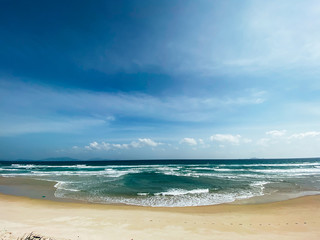 Fototapeta na wymiar Sandy seashore, calm soft waves at sea, sunny weather, blue sky with white clouds