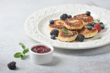 Cheesecakes with berries. Cheesecakes served with fresh berries of raspberries, blackberries and mint. Light background. Close-up. 
