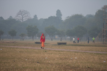 An Indian monk with vibrant attire walking on a dry grass field in a misty  winter morning. Indian lifestyle.