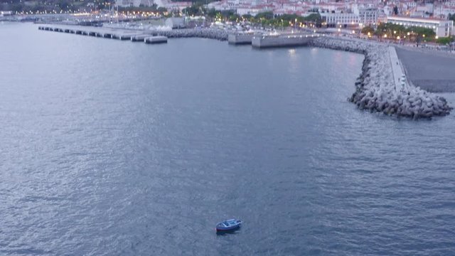 Drone footage of lonely boat floating on the ocean surface near European city of Funchal on the island of Madeira, Portugal during a cloudy afternoon