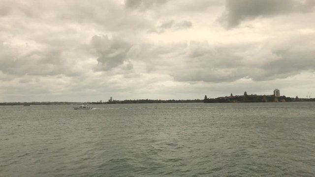 Small yacht sails across the Auckland City harbor on a grey cloudy day
