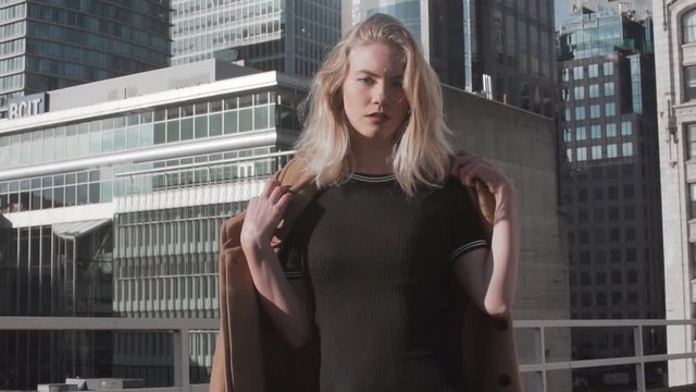 Slow-motion video of a beautiful stylish female in an urban environment. A pretty blond woman with a modern coat modeling for a fashion magazine.