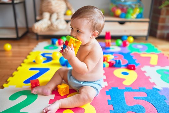Beautiful toddler sitting on puzzle carpet playing with building blocks at kindergarten